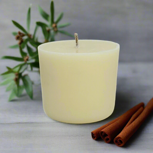 White candle with cinnamon sticks, lavender and Ylang Ylang on a light surface