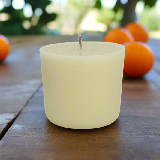 White refill candle on a wooden surface with oranges in the background